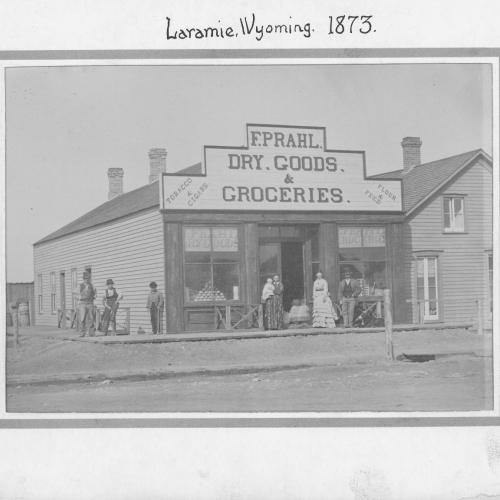 Photo, labeled "Laramie Wyoming 1873," shows wooden storefront with sign, "F. Prahl Dry Goods and Groceries / Tobacco and Cigars / Four and Feed." Several people stand on the wooden boardwalk in front.