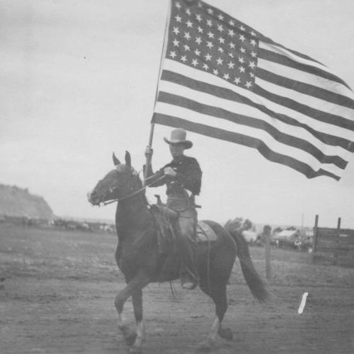 cowboy on horseback carries an American flag