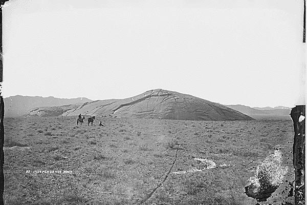 treeless plain with a low granite hill and two people riding on horseback in the distance