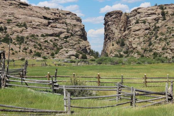 rail fences cordoning off a grassy area in front of hight rock cliffs either side of and open slot