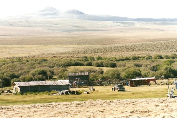 view of low-lying ranch buildings on a plain above a riverbed with rounded mountains in the distance