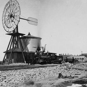 A windmill at Laramie drew water for steam locomotives, ca. 1869. Roundhouse and machine shops at back right. A. J. Russell, Wikipedia. 