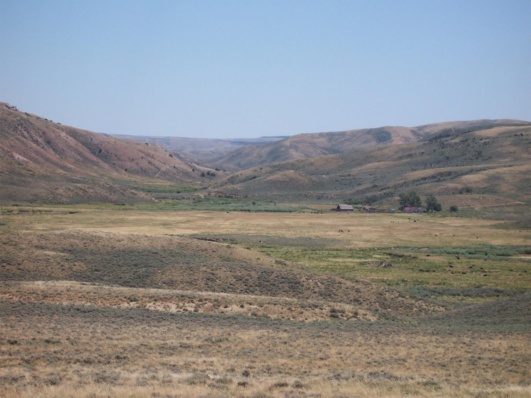 A view of Muddy Creek Canyon looking east. The Overland Trail emerged from the canyon here and continued west. The Rawlins to Baggs Road crossed the photo from left to right, passing the Sulphur Springs Ranch at right. Sulphur Springs was originally an Overland Trail stage station which was repurposed as a cattle and sheep ranch after 1868. It was also a road ranch on the Rawlins to Baggs Road. Western Archaeological Services.