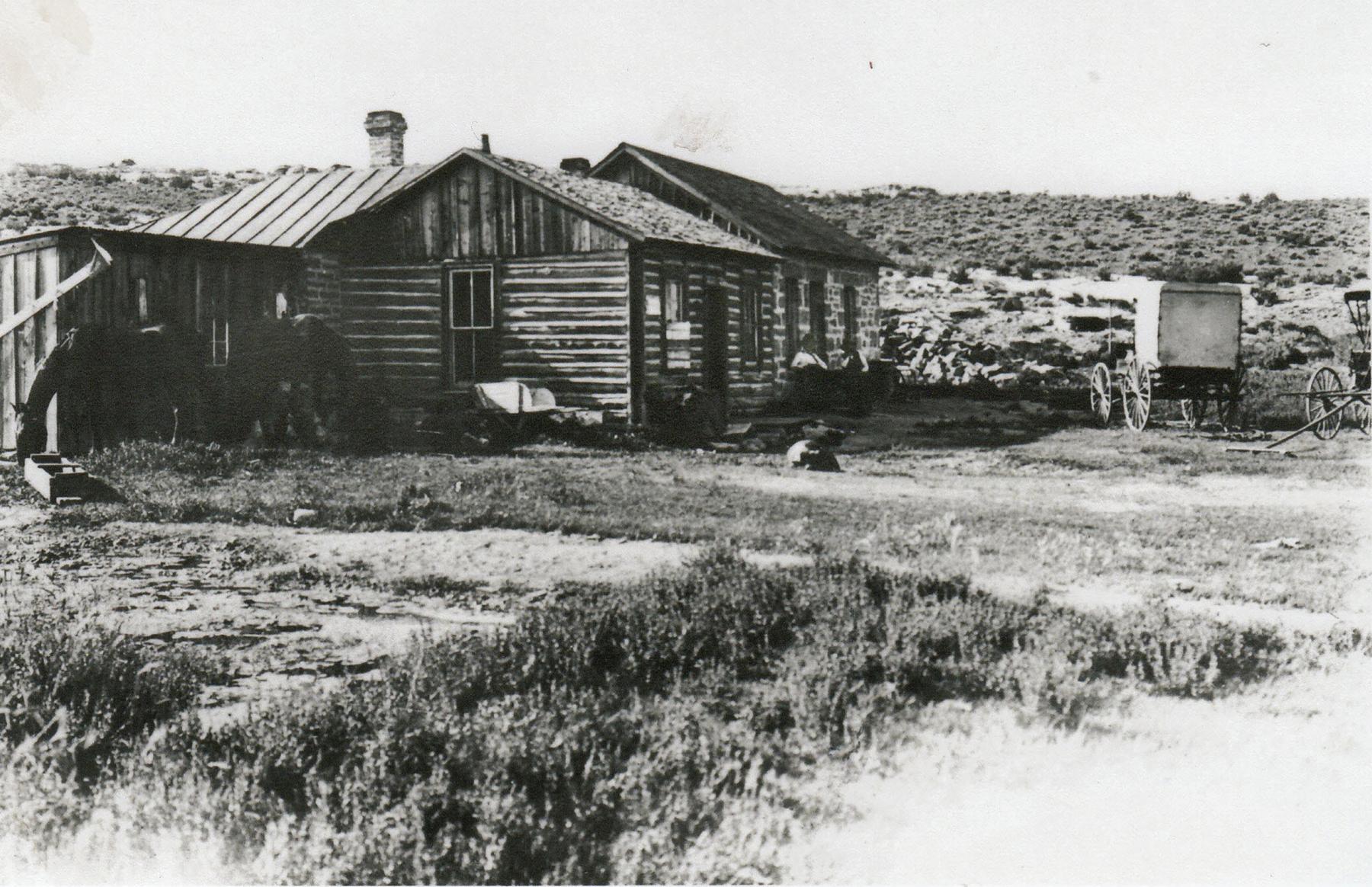 log house with addition on a treeless land, and two buggies in front