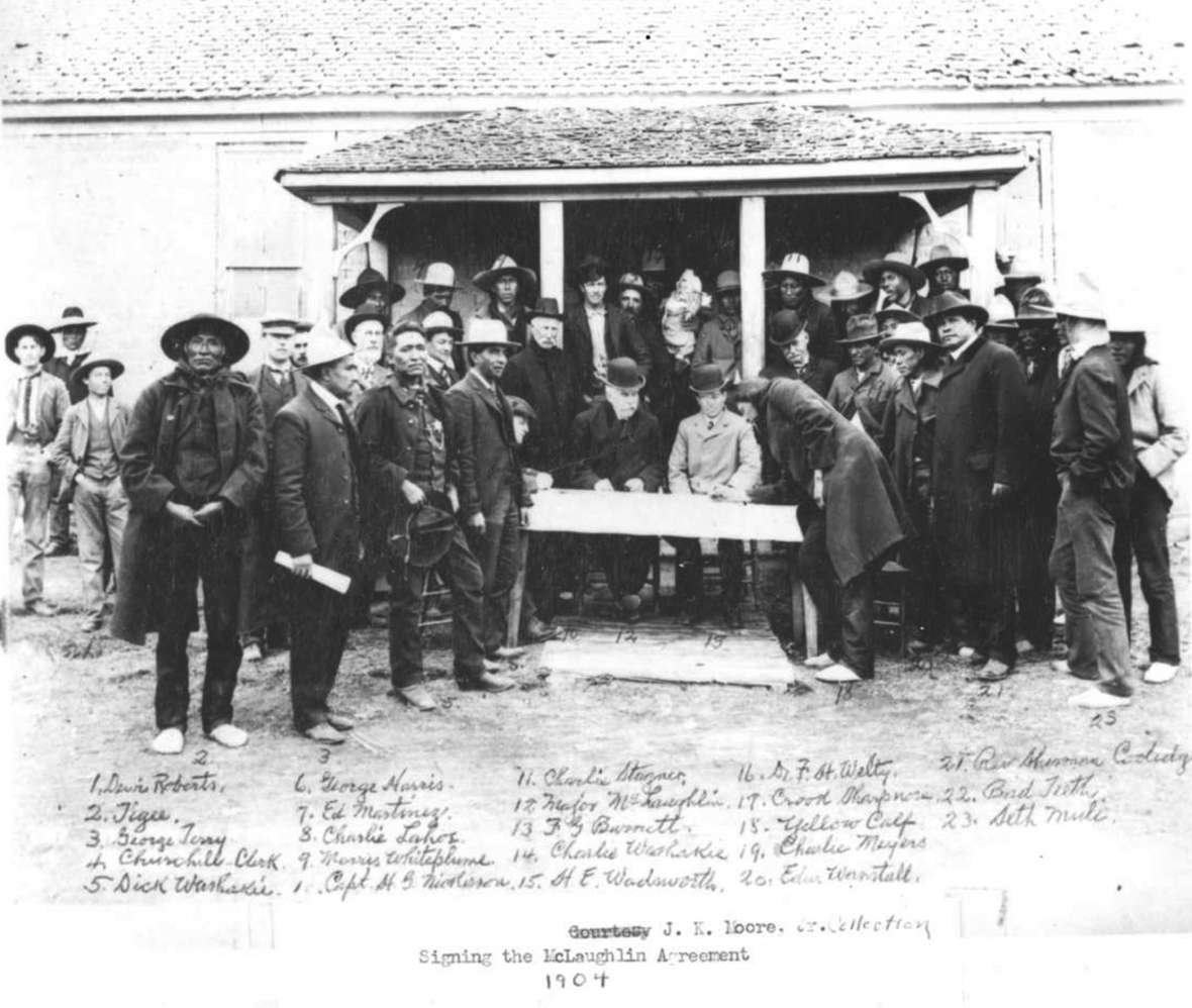Shoshone and Arapaho men voted in 1904 to cede still more tribal land to the U.S. government. Here, the Arapaho leader Yellow Calf signs the agreement. Sherman Coolidge, at right in long black coat, was a prime proponent of the cession. American Heritage Center.