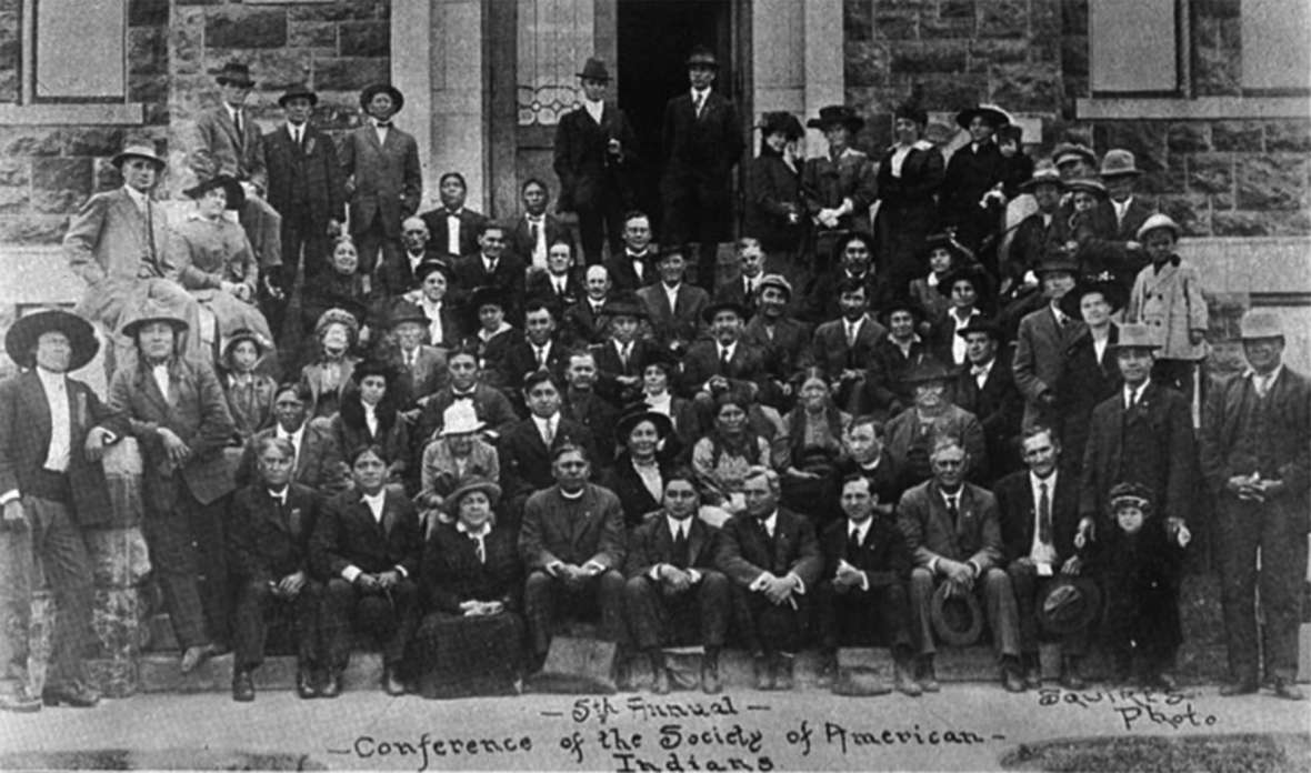 Attendees at the fifth annual conference of the Society of American Indians, 1915. Sherman Coolidge, in clerical collar, is near the center of the front row. His time in the Society softened his views on assimilation considerably, and he began to view Indian cultures as valuable. Wikipedia. 