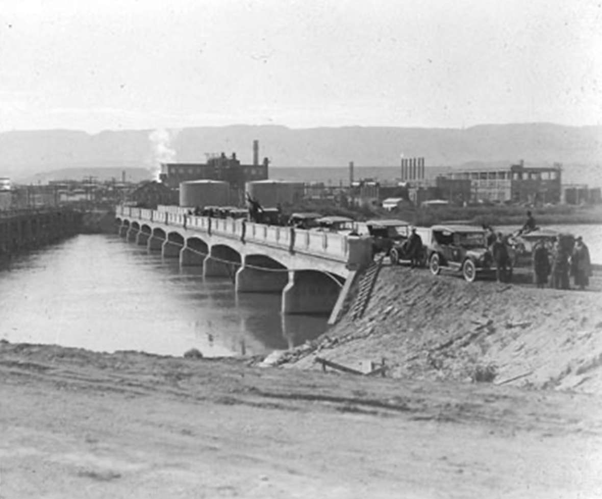 The 1920 Park-to-Park caravan paused in Casper, Wyo., on a new concrete bridge over the North Platte, with the Midwest Refinery and Casper Mountain in the background. Park County Archives.