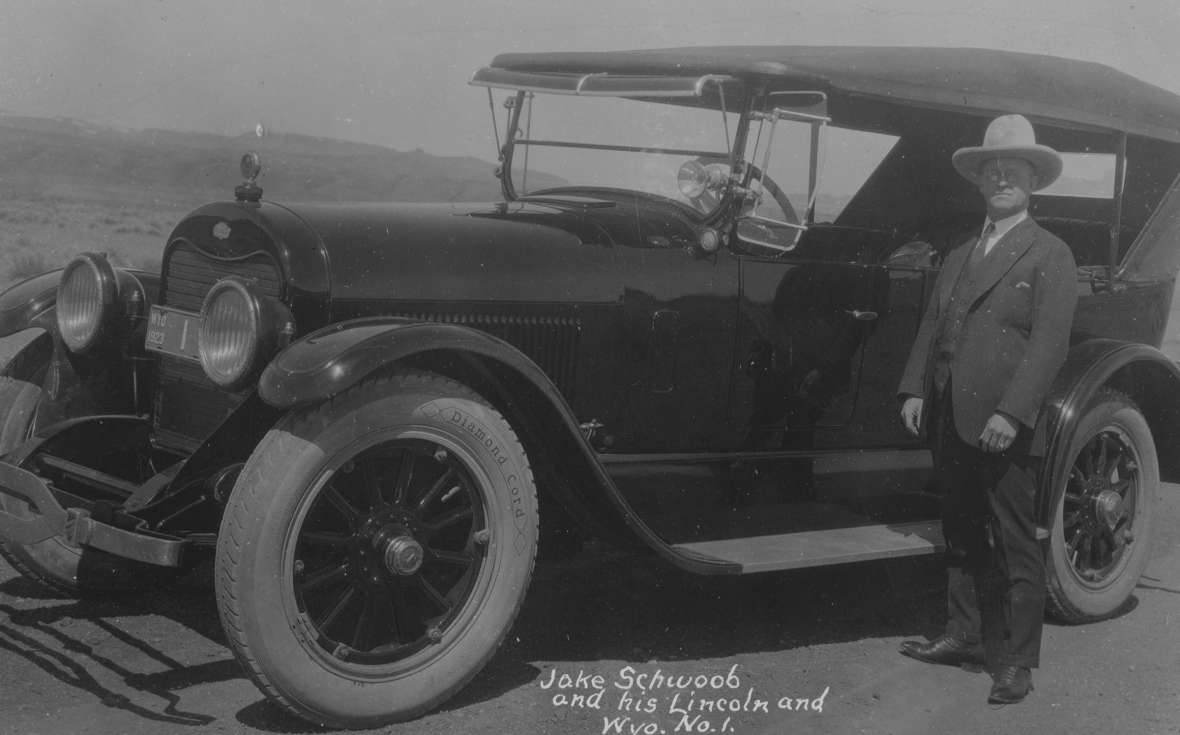 Good roads promoter Jake Schwoob of Cody owned one of Wyoming’s first car dealerships, and developed the county-based numbering system for Wyoming license plates. Here he is in 1923 by his Lincoln, bearing Wyoming license plate #1. American Heritage Center.