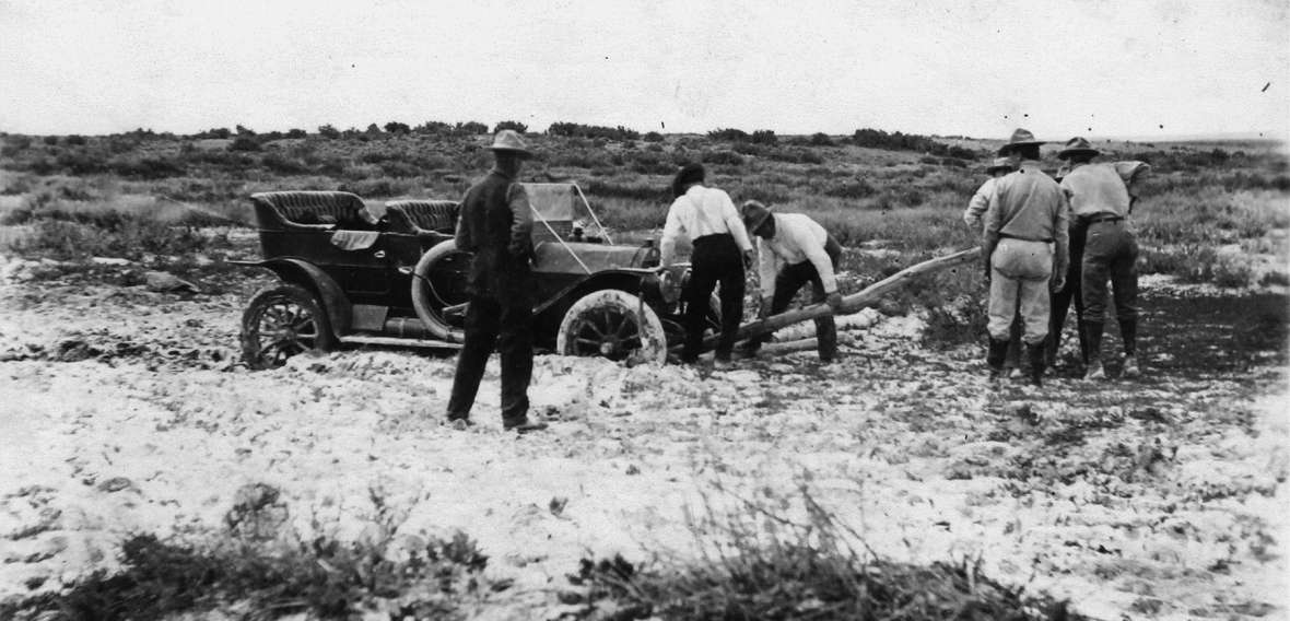 Seven men work to move a car out of the mud on the Lincoln Highway north of Laramie, Wyo., about 1915. In the early years of its existence, the highway was mostly an idea. Laramie Plains Museum.