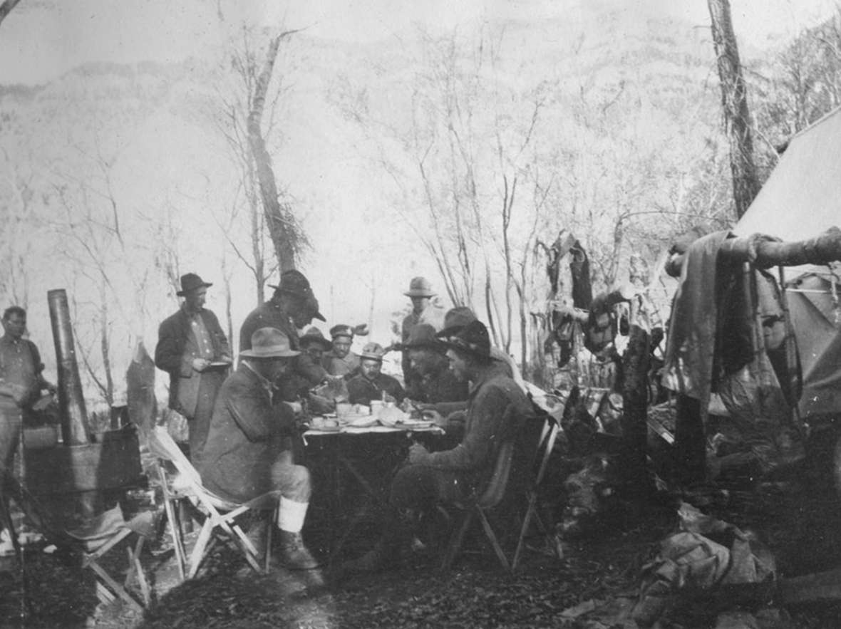Charles “Spend-a-Million” Gates, at the head of the table, and his hunting party eat a meal prepared by the camp cook on their guided hunt into the Thorofare wilderness, October 1913.. Park County Archives.