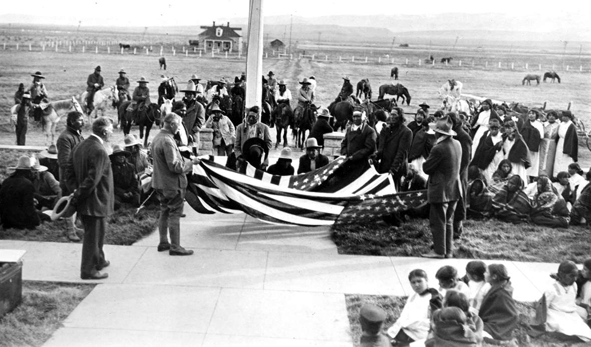 The citizenship expedtion's flag raising ceremony at Fort Washakie, Wyo., October 1913, with Shoshone and Arapaho people on hand. Joseph Dixon holds the near corner of the flag. Wyoming Veterans Memorial Museum.