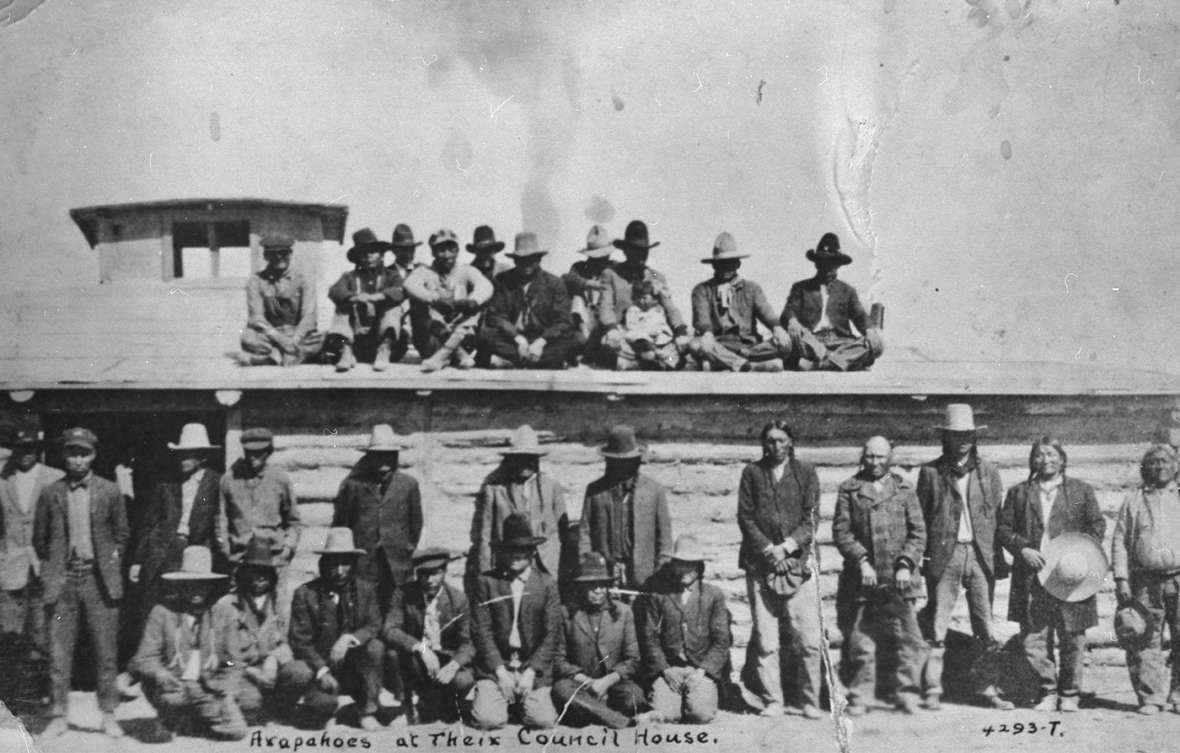 The log council house was used by both the Eastern Shoshone and Northern Arapaho tribes. Shown here—an Arapaho gathering. Riverton Museum.