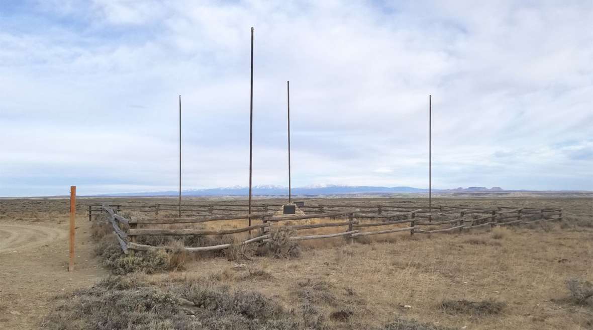 A view to the north at the Tri-Territory Historic Site. The poles are for the flags of Britain, Mexico, France, and, on the stone monument, the United States. The Wind River Range is visible in the distance, with the Oregon Buttes on the horizon on the right. Author photo.