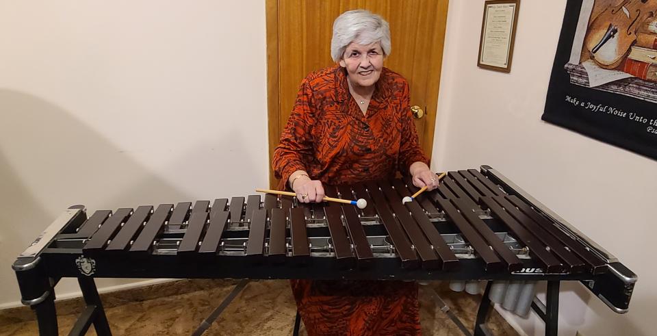 Woman in a red dress, holding mallets, stands behind marimba