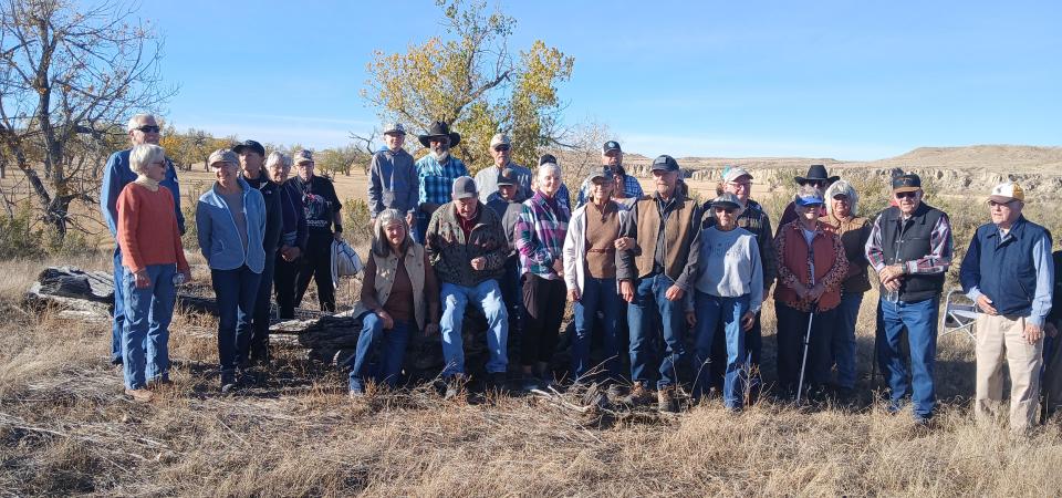 A group of about 20 people pose on a dry prairie site