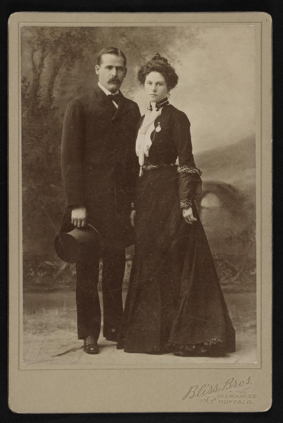 Man in a suit and woman in a long black dress pose together for a professional portrait