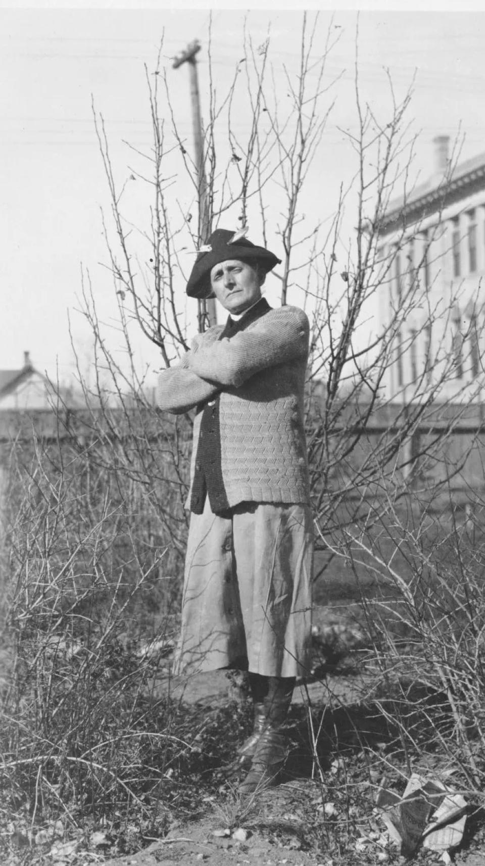 garden portrait of a person in culottes, a cardigan, and what looks like a tri-cornered hat, with arms crossed over the chest