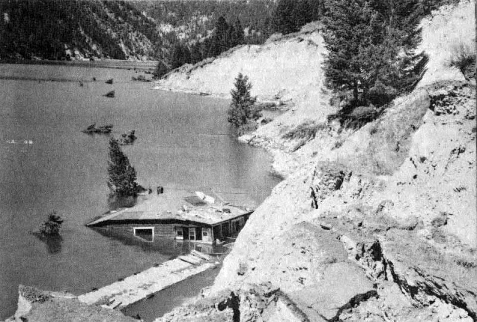 Grace Miller jumped out of her front door across a large 5-foot crevice, just before her home fell into Lake Hebgen. (National Forest Service) The edge of a lake whener a cabin tilts into the water, which rises to its roofline on one side