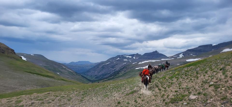 Trail through a vast wide-open mountain landscape without trees, patches of snow dotting ridgelines 