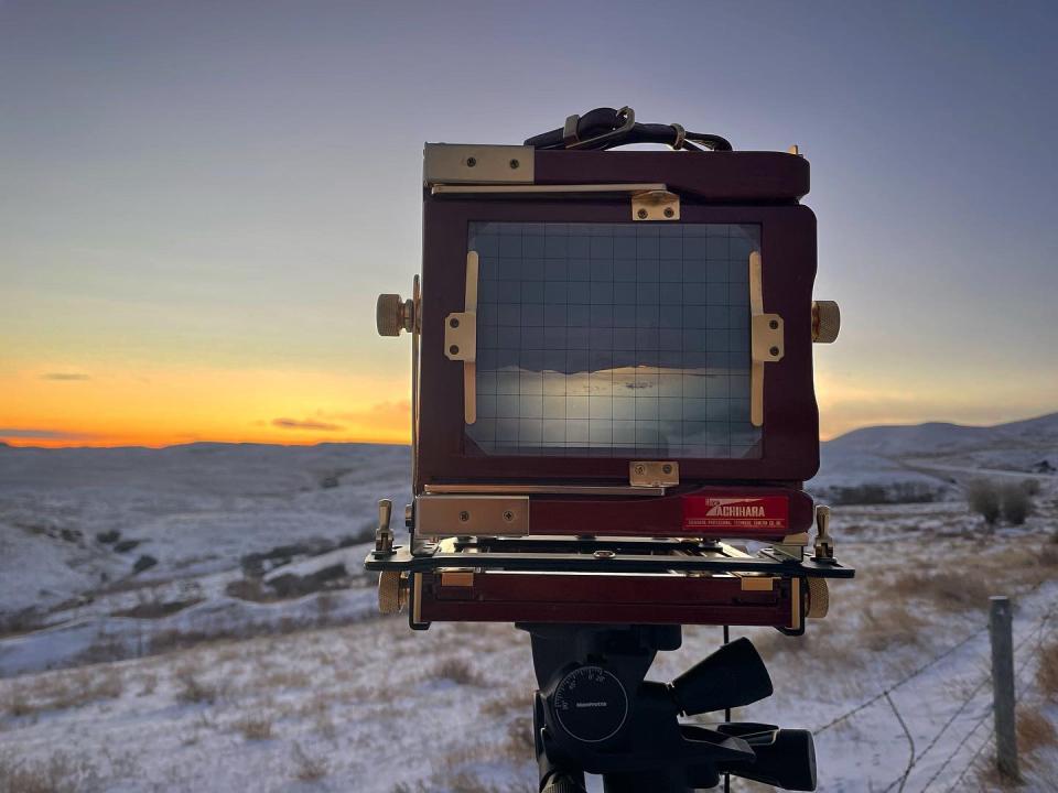 closeup of the large format camera, focused on the landscape before it, as the sun rises in the distance