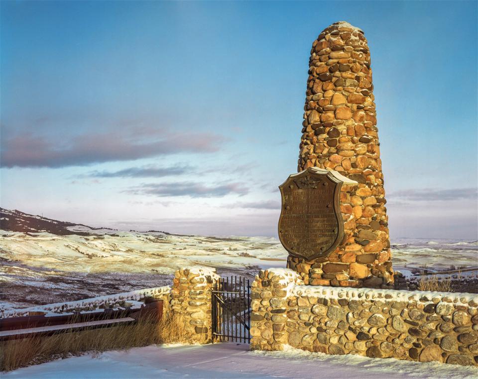 a stone monument about two stories high with a shield-shaped information panel stands at the edge of a rolling sagebrush plain
