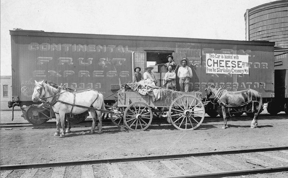 Men pose on a horse-drawn wagon in front of a railroad car, with a sign on the side stating "This car is loaded with cheese from the Star Valley Creamery, Afton, Wyo"