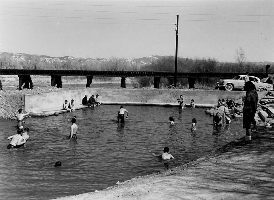 Young people in a large walled-off pool by a river with a bridge in the background