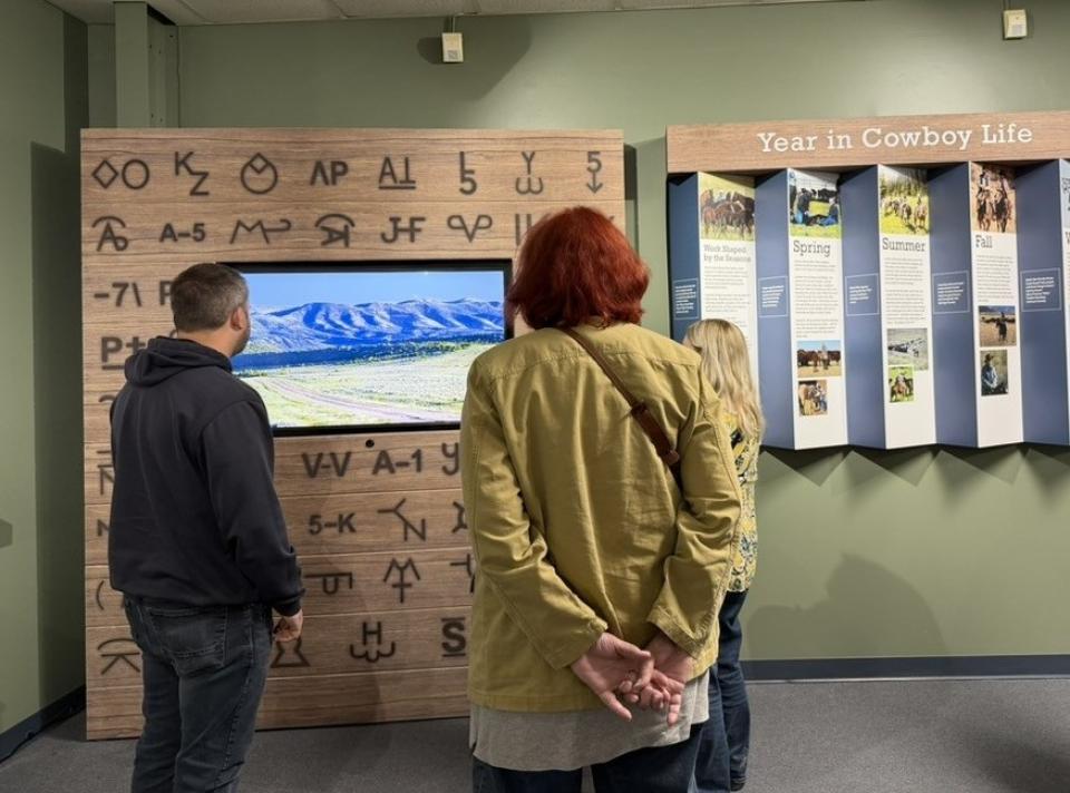 People stand in front of a wall display and video with reproductions of cattle brand images