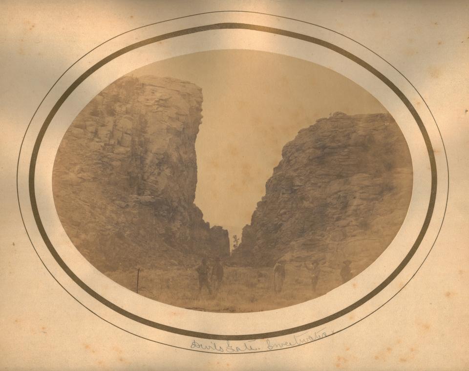 sepia-toned photo of several people standing before a deep cleft in a cliff