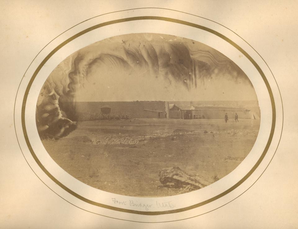 sepia photo across an open, treeless space to a long, low windowless building with a few scattered figures