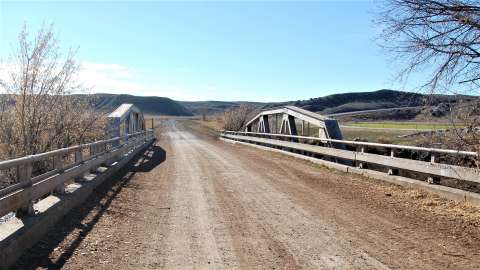 In 1936, the Black and Yellow Trail was reconstructed in the vicinity of Ten Sleep. Portions of the road were realigned, and this single-span Warren pony truss bridge was built to cross the Nowood River just west of Ten Sleep.  This route (now Washakie County Road 580A) was abandoned in the 1960s when a new road was built a few hundred feet to the north.  One can still drive this county road west toward Worland for several miles to a point where drainages and topography make the road impassable. Authors photo,  2013.