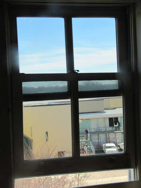 A view of the Lorraine Motel balcony where King died, through the boardinghouse window from which James Earl Ray is believed to have fired the fatal shot. Wikimedia Commons.