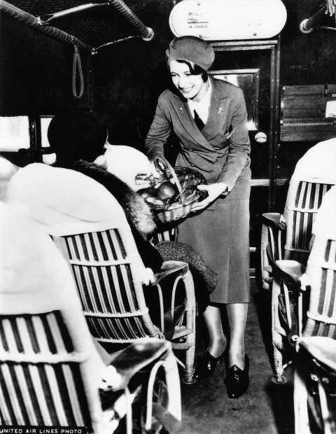An unidentified stewardess serves food to passengers in wicker chairs bolted to the floor of a Boeing Model 80A aircraft, ca. 1930. United Air Lines Archives. 