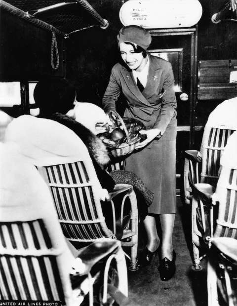 An unidentified stewardess serves food to passengers in wicker chairs bolted to the floor of a Boeing Model 80A aircraft, ca. 1930. United Air Lines Archives.    