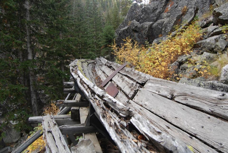 An intact segment sweeps around the first large curve near the west, or upper, end of the flume. Portions of the walkway also remain, as do sporadically placed steel plates used to reinforce or patch the wooden structure. E. Rosenberg, 2010.