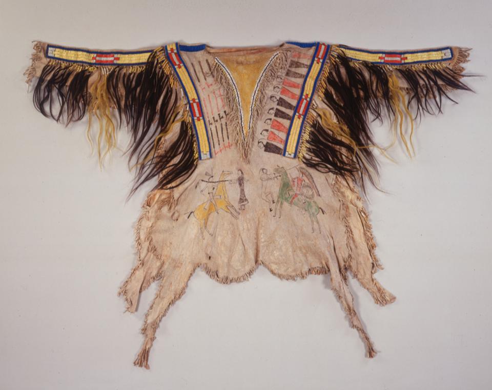 Back view of a Cheyenne man’s shirt, ca. 1860. The painted design illustrates two Cheyenne warriors battling Pawnee fighters. Painted pipes represent the number of war parties led by the artist of the shirt and the row of figures represents enemies he has defeated. Shown on the front is the image of the Cheyenne warrior defeating two Crow enemies. Other decorations include horse and human hair, porcupine quills and glass beads.  NMAI, Smithsonian Institution, catalog Number: 8/8034. 