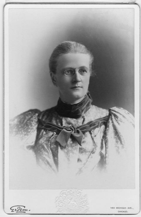 fromal portrait of woman wearing glasses and a puffy-sleeved floral dress with velvet collar and bow