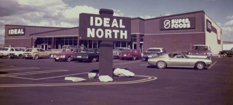 Large brick building surrounded by a parking lot with prominent "Ideal North" sign in the foreground