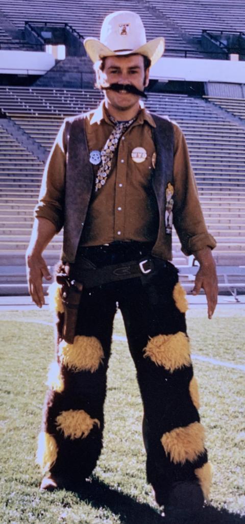man wearing exaggerated cowboy gear: hat, vest, chaps, boots