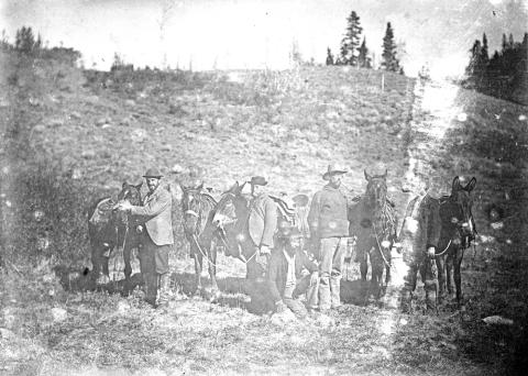 four men posing with horses and mules in front of a sagebrush hillside