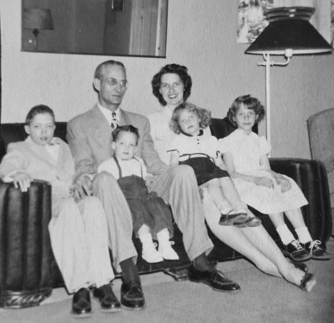 A couple holds four young children on a sofa