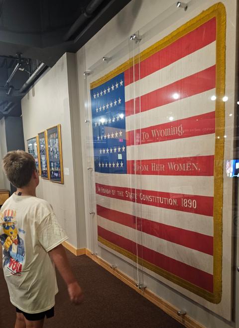 A child wearing a Wyoming 250 Fourth of July shirt looks at the 44-star flag from 1890 on display at the Wyoming State Museum.