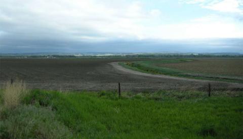 open treeless plain, fenced in the foreground, with tilled land beyond